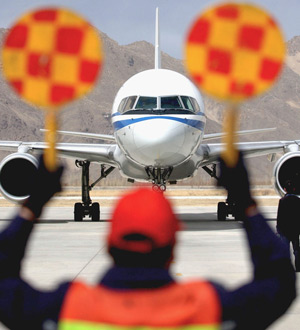 An airport staff directs an aircraft into position