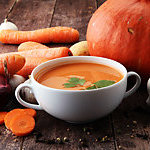 Pumpkin and carrot soup with cream and parsley on dark wooden background.