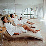 Two women in white robes relaxing at hotel spa.