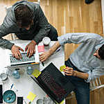 Overhead view of 2 developers talking and working on their laptops.