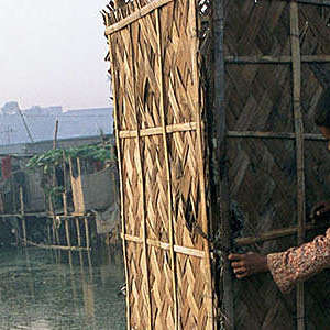 Third-world child tries to open the door of an outdoor toilet cubicle that is built on stilts over water