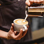 Close up view of the hands of a barista preparing a coffee by drawing a flower with milk.