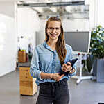 Portrait of a businesswoman with eyeglasses standing in office. Female entrepreneur looking at camera and smiling holding a digital tablet.